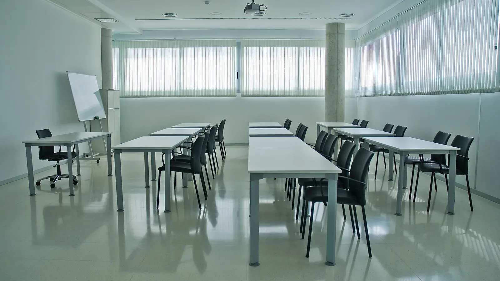 Boş, modern bir toplantı/eğitim salonu — düzenli sıralanmış masalar, sandalyeler ve bir beyaz tahta